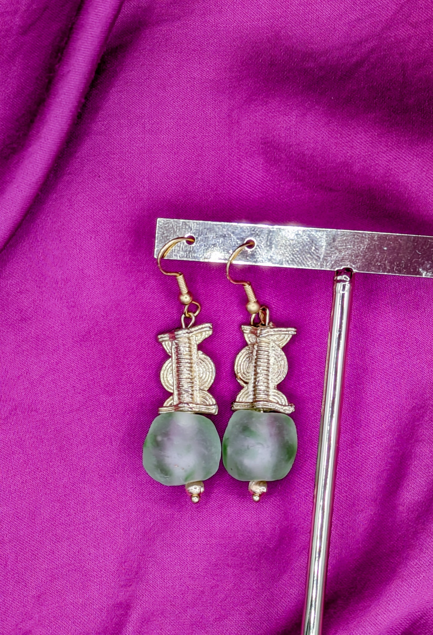 Ces boucles d'oreilles réalisées artisanalement sont composées d'une perle translucide vertes d'eau ainsi qu'une perle doré ( poids Akan ) en laiton.