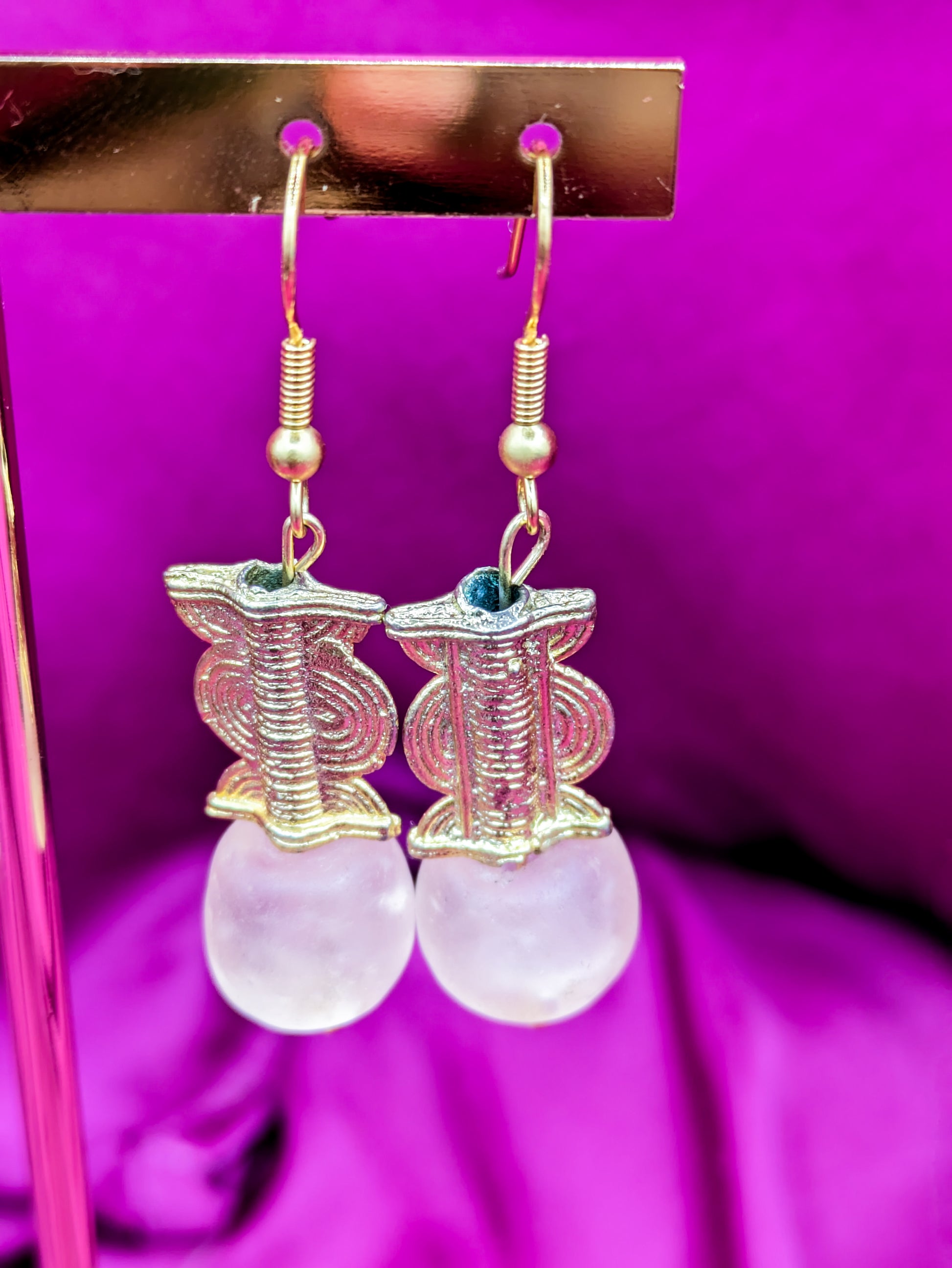 Boucles d'oreilles composées d'une perle translucide rose ainsi qu'une perle dorée ( poids Akan ) en laiton.