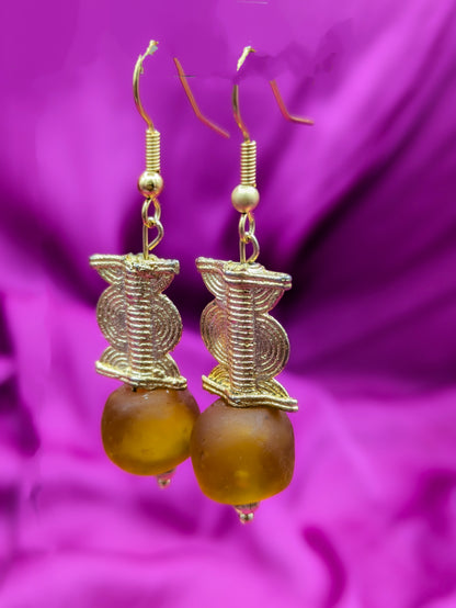 Ces boucles d'oreilles composées d'une perle translucide brunes ainsi qu'une perle doré ( poids Akan ) en laiton. 