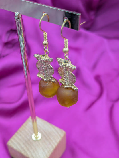 Ces boucles d'oreilles  composées d'une perle translucide brunes ainsi qu'une perle doré ( poids Akan ) en laiton. 