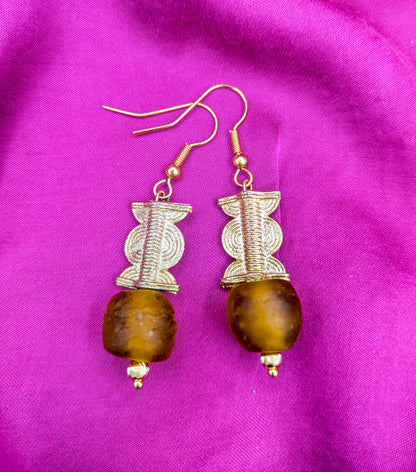 Ces boucles d'oreilles composées d'une perle translucide brunes ainsi qu'une perle doré ( poids Akan ) en laiton. 