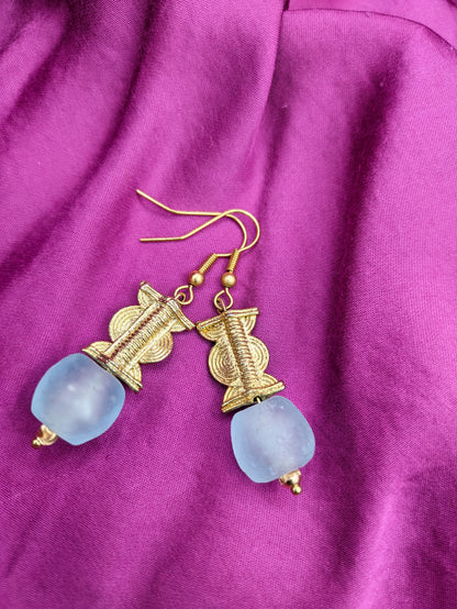 Ces boucles d'oreilles réalisées artisanalement sont composées d'une perle translucide bleue pastel ainsi qu'une perle doré ( poids Akan ) en laiton. 